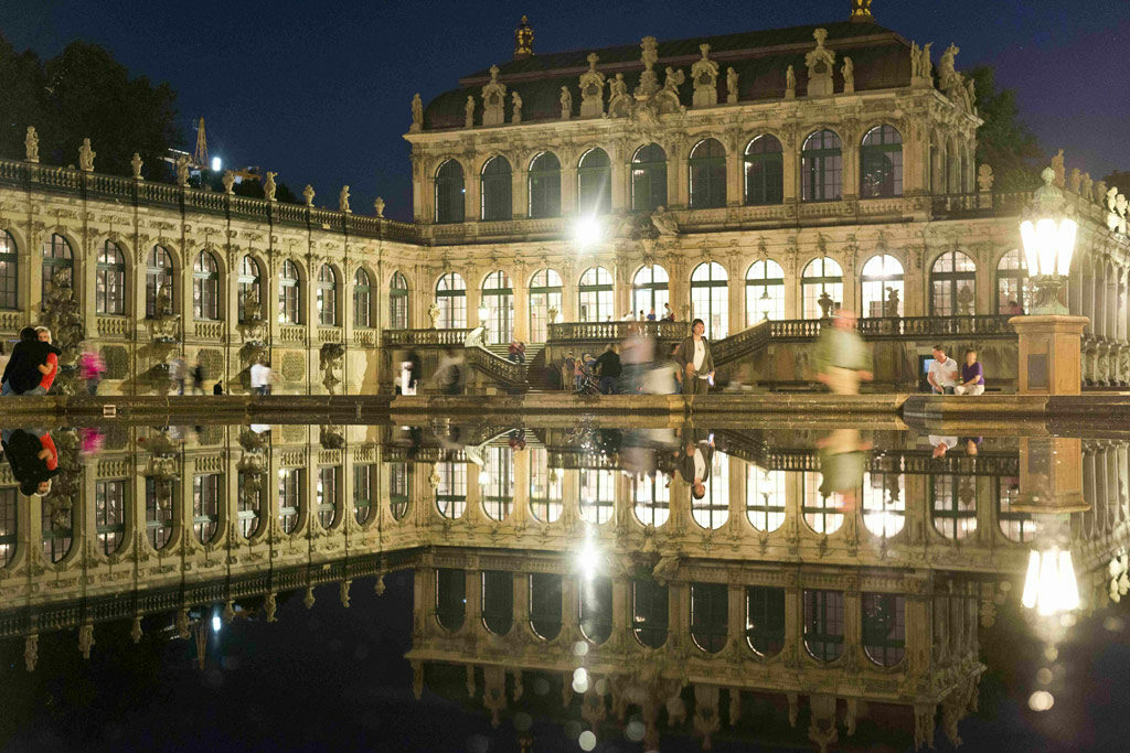 Zwingerhof mit erleuchteten Fenstern nachts im Wasserbecken gespiegelt