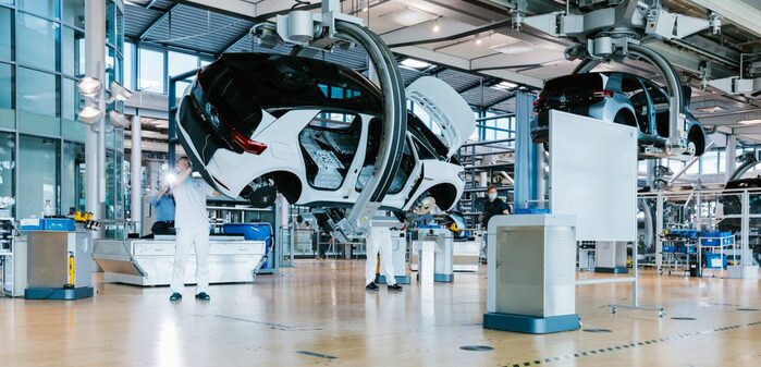 Die Montagehalle. Ein Auto befindet sich in der Fertigung. Es wird von einem Roboterarm gedreht und in der Luft gehalten.