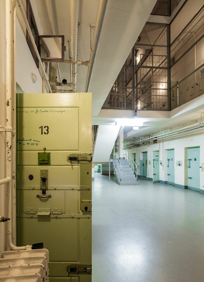 Blick in das Hafthaus, auf eine geöffnete Zellentür, Flür mit Zellentüren und Blick auf vergitterte Umgänge der oberen Etagen