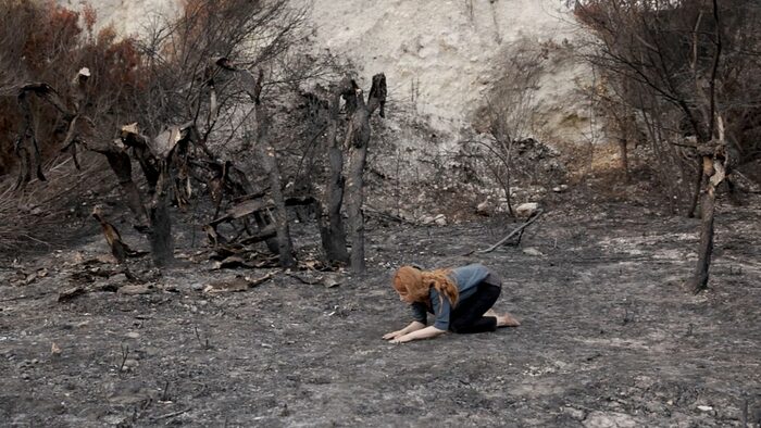 Eine Frau kniet in einer durch Feuer verwüsteten Landschaft