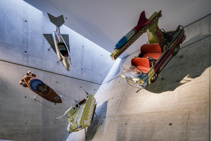 Blick auf eine schräge Wand in der Ausstellung, darauf angebrächt verschiedene Fluggeräte und Fahrzeuge