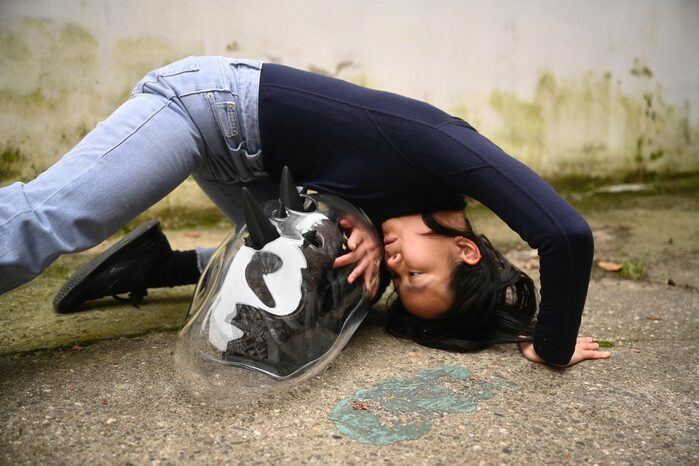 Eine Frau kauert auf Asphalt, gebeugt über eine schwarz-weißen Gegenstand in einer durchsichtigen Plastikumhüllung.