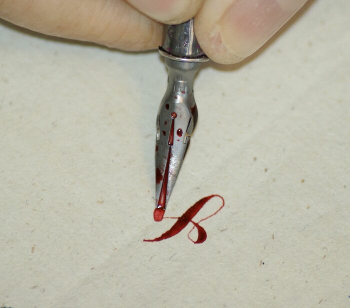 Finger führen eine alte Schreibfeder und schreiben einen Buchstaben in leuchtend roter Tinte