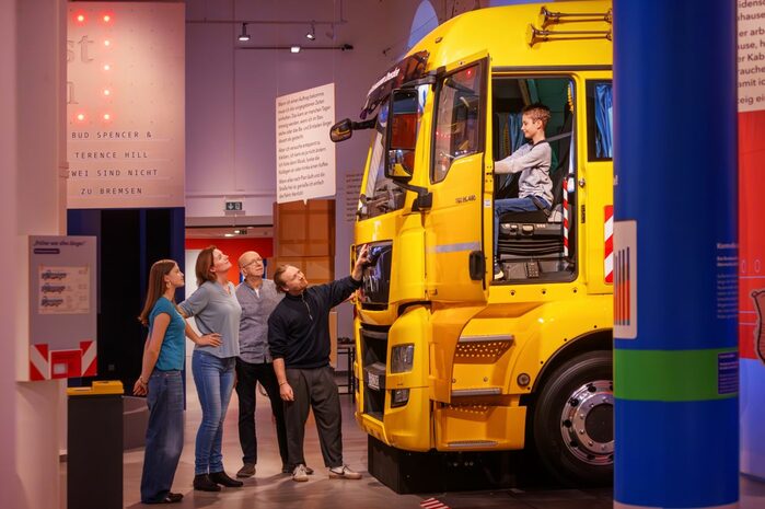 Ein knallgelber Lastwagen mitten im Museum. Ein Junge sitzt am Steuer.