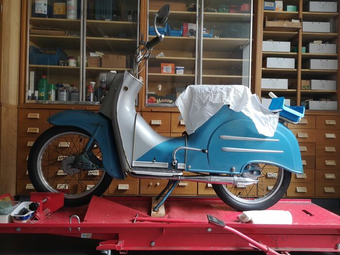 Auf einem Tisch steht ein alter heller Motorroller.