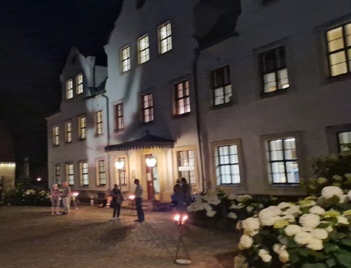Blick in den nächtlichen Schlosshof mit Menschen. Licht fällt aus den Fenstern.